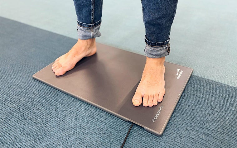 A man in blue jeans standing barefoot on the Materialise Footscan Pro Level pressure plate.