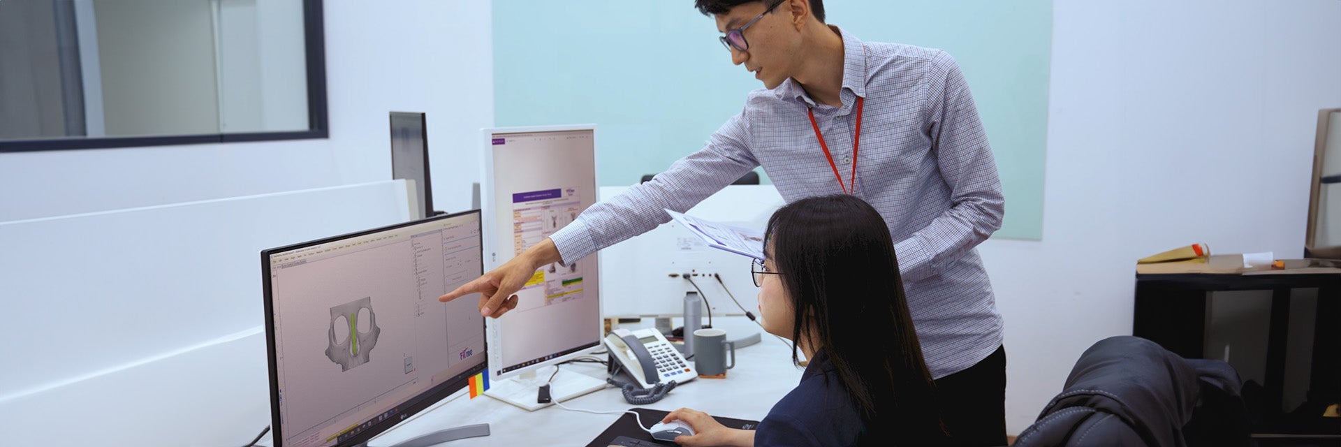 Man pointing to a computer with medical software while speaking to a woman sitting at a desk
