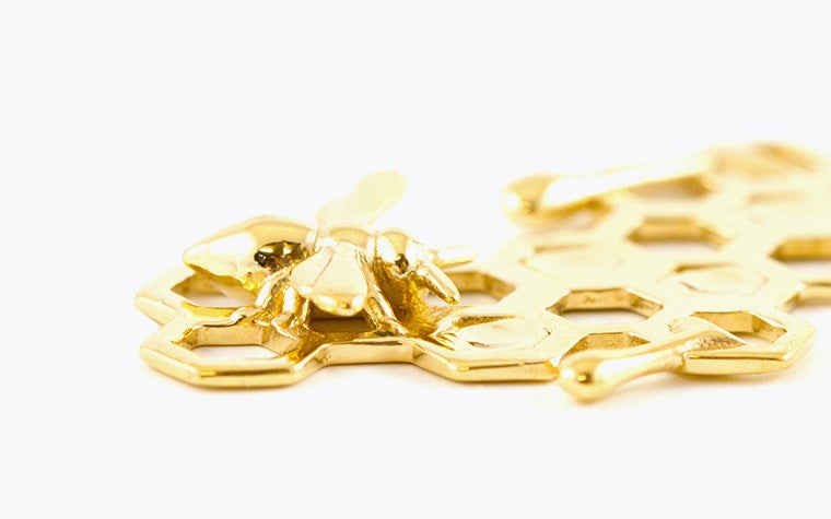 A gold charm in the shape of a honeybee and honeycomb made with lost-wax casting.