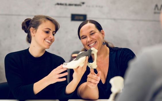 Two women smiling and looking at a 3D-printed part