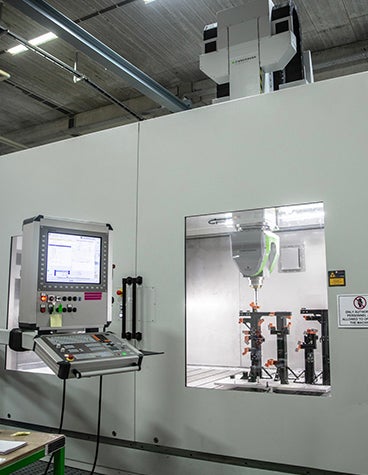 Control panel of a CNC milling machine, beside a window where the worker can see the machine at work. 