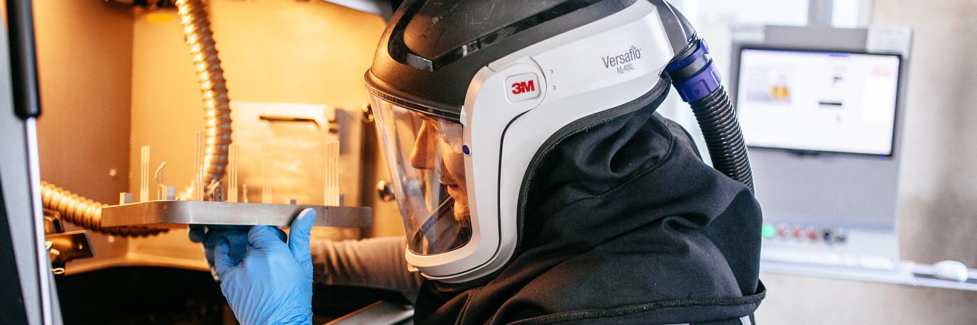 Man wearing safety gear and removing a 3D-printed build from a 3D printer