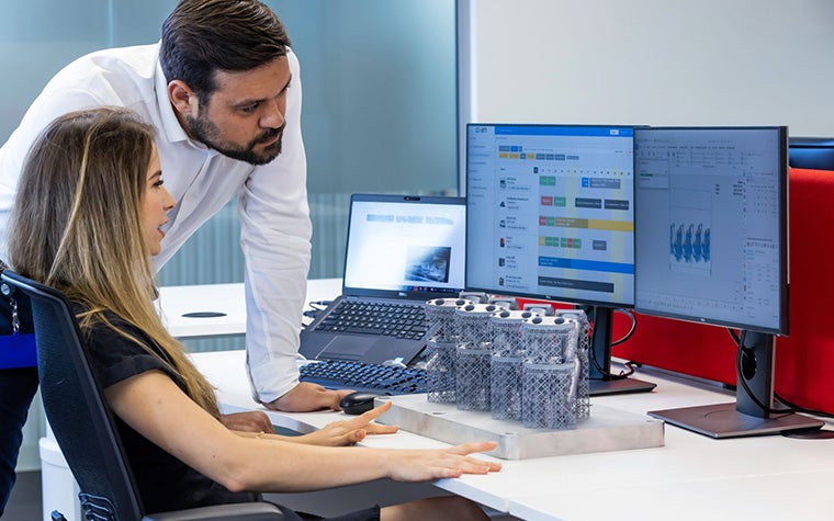 A man and a woman staring at a desktop computer screen displaying the e-Stage for Metal+ software.