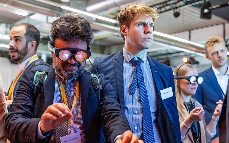 Man wearing AR goggles at the 3D Printing in Hospitals Forum 2024 and holding his hands in front of him. He stands in a group of people also wearing goggles or observing