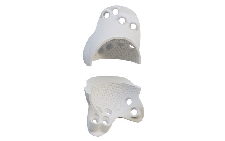 Two separate white implant trial components with textured inner surfaces and multiple circular openings, representing superior and inferior sections for acetabular preparation.