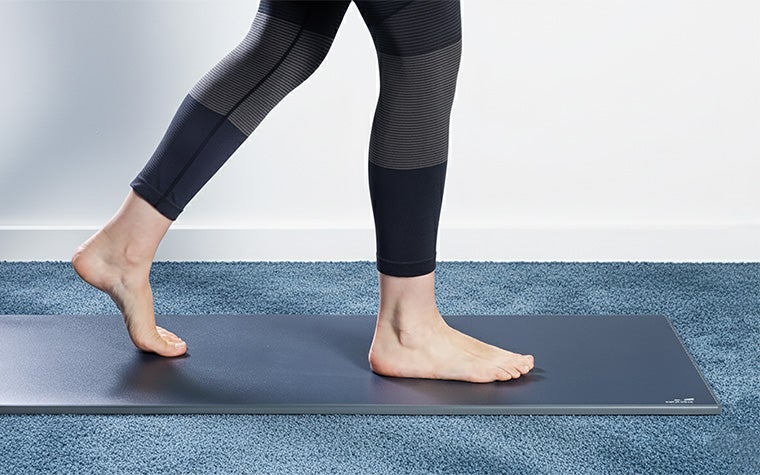 A barefoot woman walking on the Materialise Footscan Pro Level pressure plate in a room with blue carpet.
