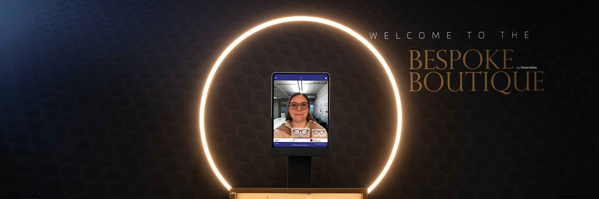 Un iPad con el programa Eyewear Fitting Suite se encuentra en un soporte rodeado de una luz selfie. La pantalla muestra el rostro de una mujer, junto con una imagen generada de unas gafas impresas en 3D.