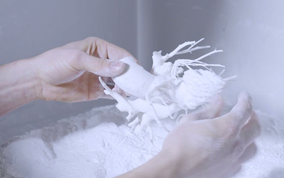 Person taking cardiac 3D-printed anatomical model out of 3D printing powder 