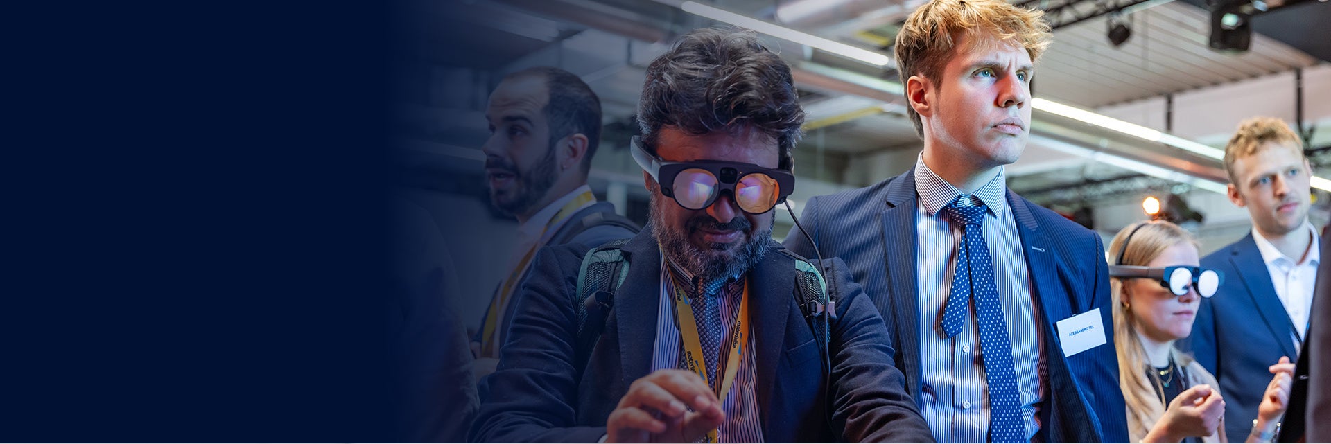Man wearing AR goggles at the 3D Printing in Hospitals Forum 2024 and holding his hands in front of him. He stands in a group of people also wearing goggles or observing. The image fades in from black on the left