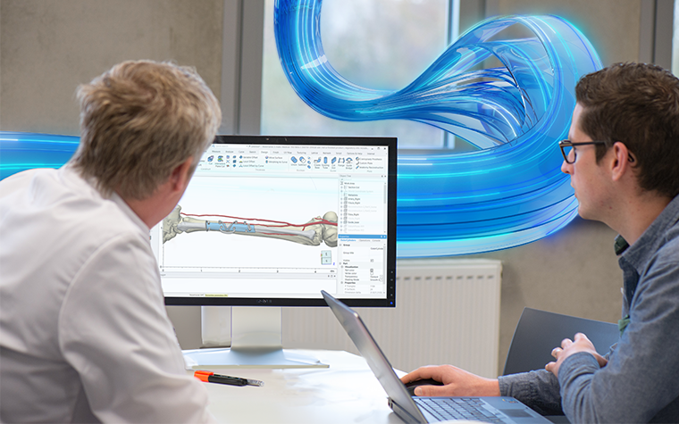 Two men sitting at a table and looking at Materialise Mimics software on a computer screen, displaying a cutting guide design on a patient bone with blue swirly lines in the background
