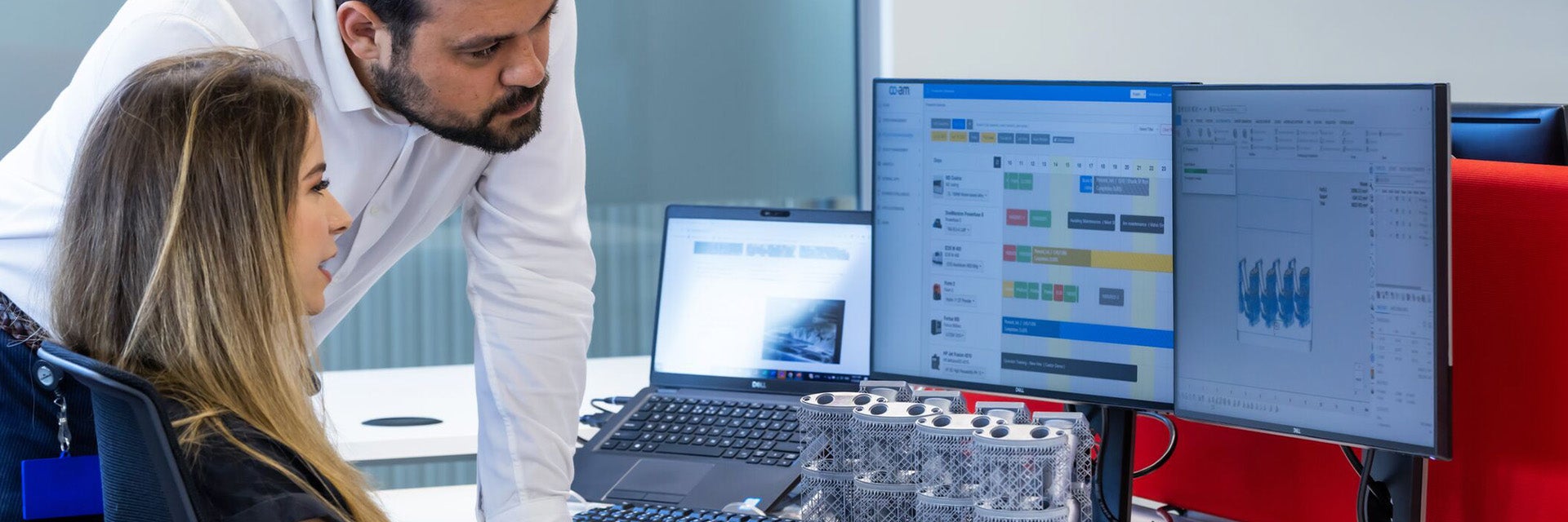 A man and a woman staring at a desktop computer screen displaying the e-Stage for Metal+ software.