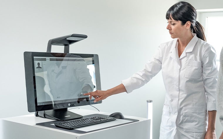 A foot health clinician in a white coat pointing at a computer screen showing the Materialise Footscan software.
