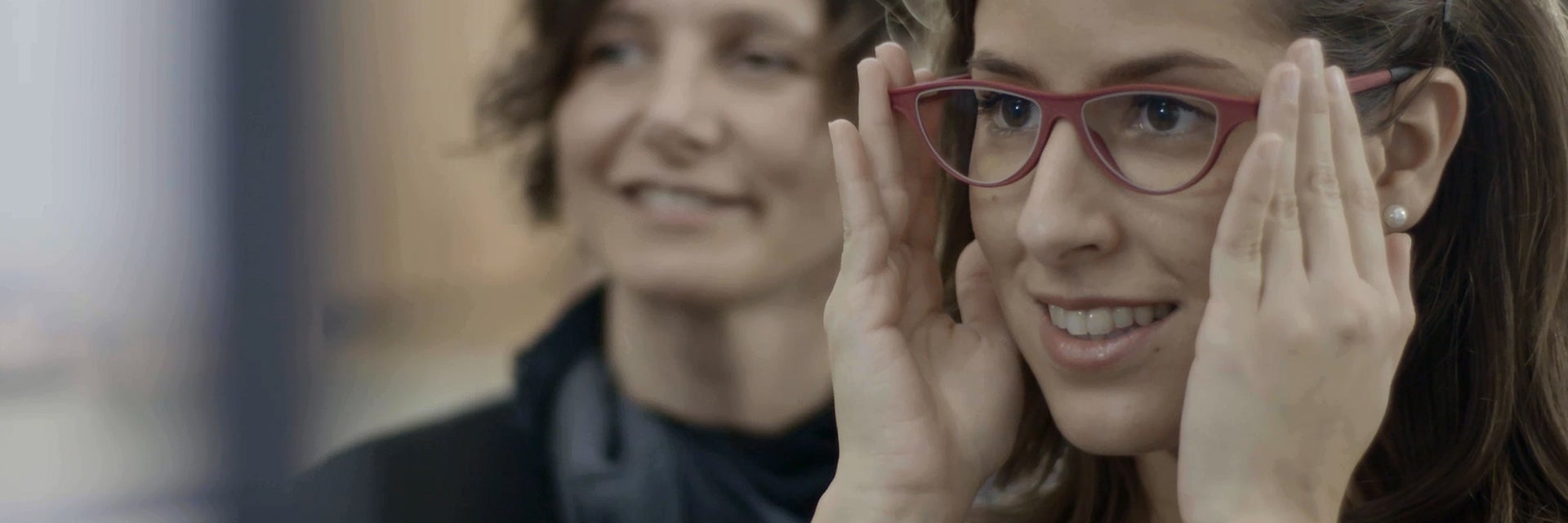 Customer trying on glasses with an optician watching in the background