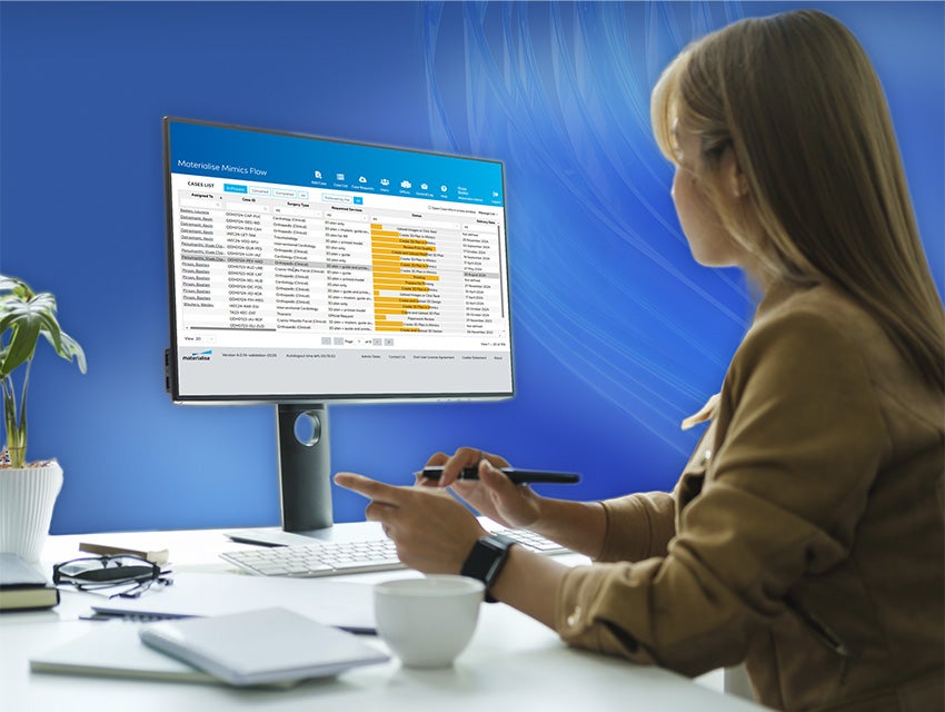 Woman sitting at a desk and looking at patient cases in Mimics Flow software with blue swirly lines in the background