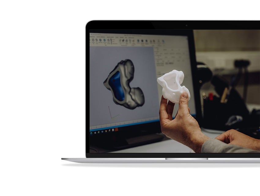 A hand holding up a 3D-printed anatomical model in front of a laptop screen with Mimics open.
