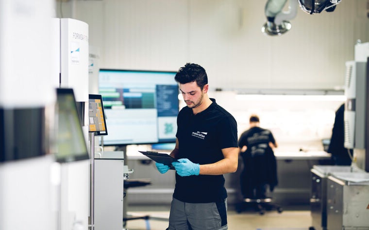 Ein Mann steht auf dem Boden einer Produktionsstätte und schaut auf ein Klemmbrett