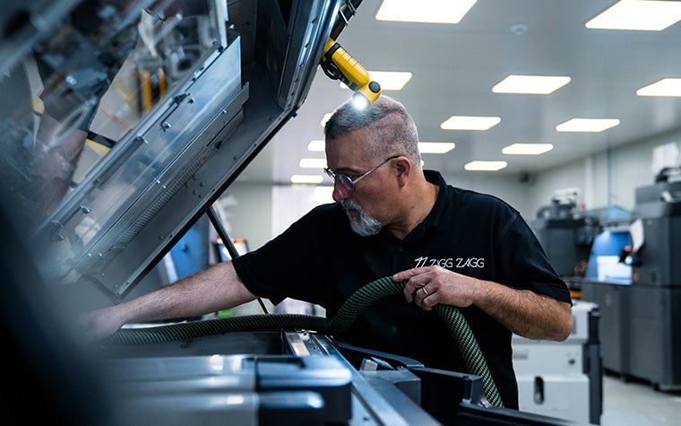 ジグザグの黒いTシャツを着た男性が、3Dプリンターの材料を掃除機で吸い取っている。