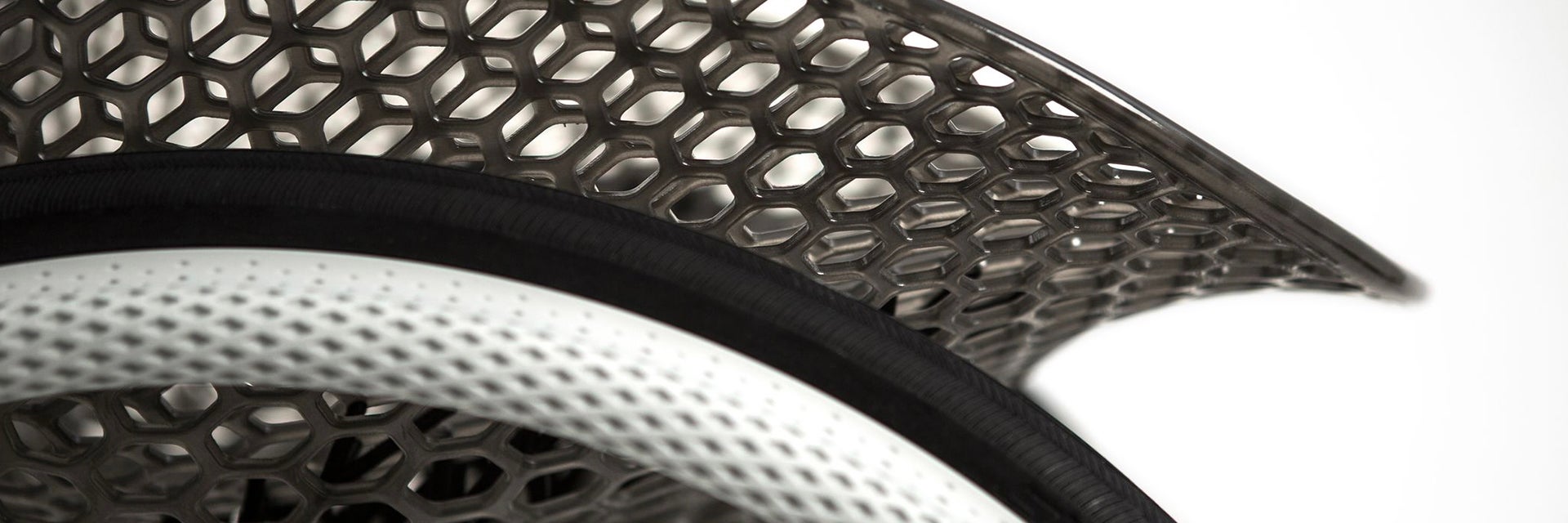 Close-up view of a geometrical, 3D-printed chair seat from a 3D-printed prototype of a customized, futuristic-looking wheelchair, using multiple 3D printing materials. The seat is lattice-structured and made of a translucent gray resin. The wheel spokes are made of 3D-printed metal.