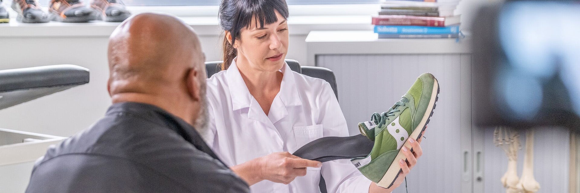 A podiatrist shows a patient how to insert a 3D-printed phits insole into a running shoe.