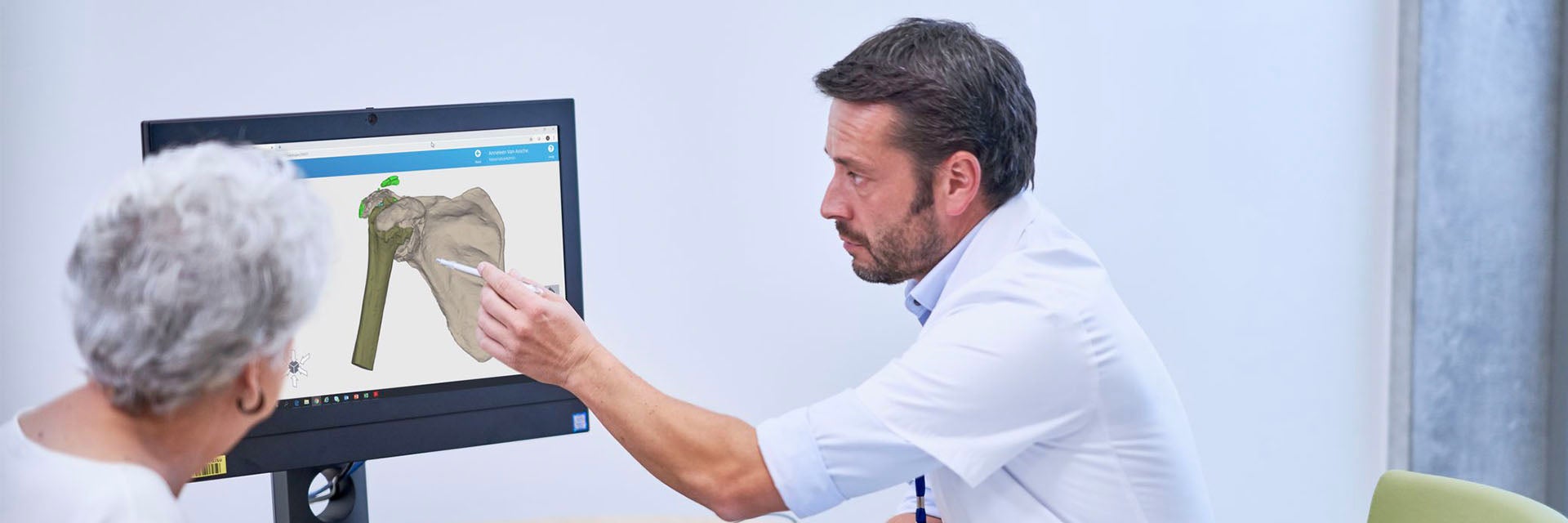 Doctor showing an elderly female patient a 3D digital model of a bone on a computer screen