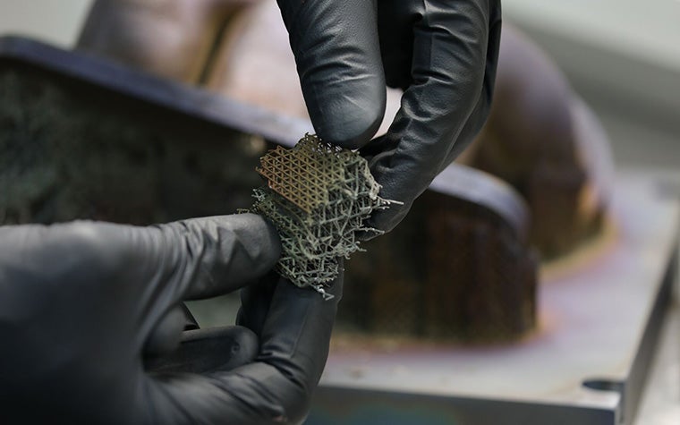 3Dプリントされた金属製の小さな正方形を持つ手袋をはめた人。