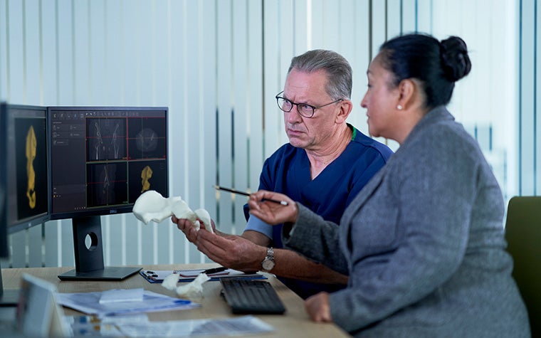 Two healthcare professionals looking at images of patient anatomy on computer screens while holding a 3D-printed anatomical model