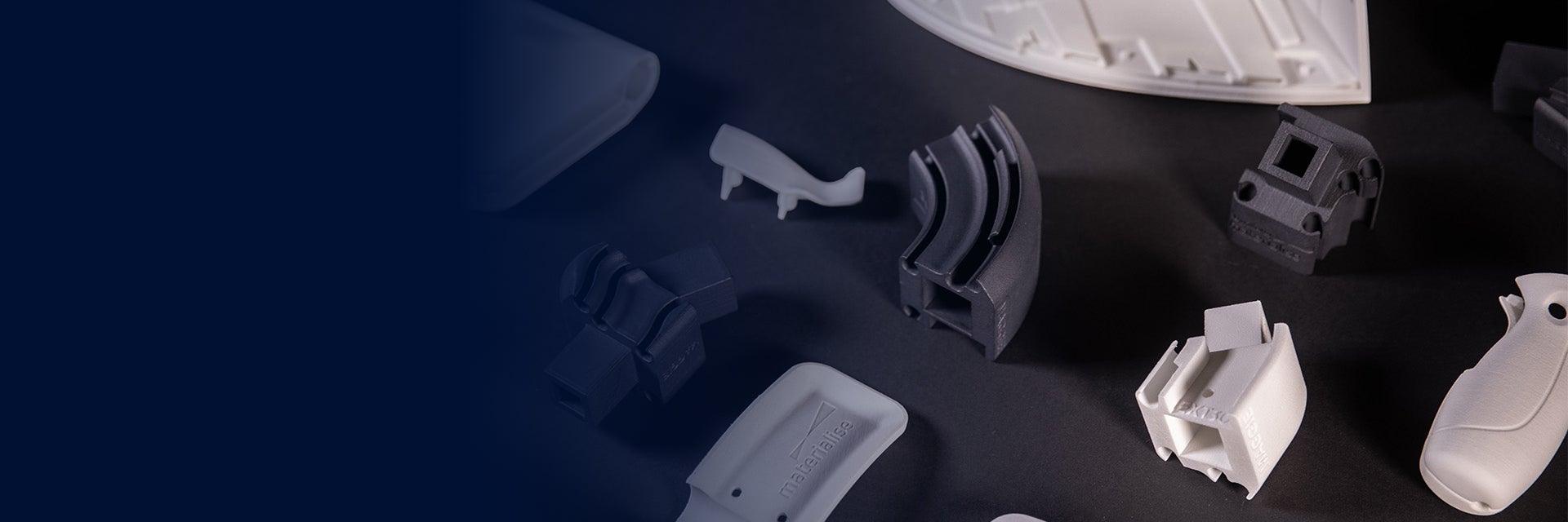 Various black and white 3D-printed parts spread out on a black table, printed with the Bluesint PA 12 technology