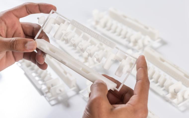 Die Hände eines Mannes halten ein weißes 3D-gedrucktes Kunststoffteil.