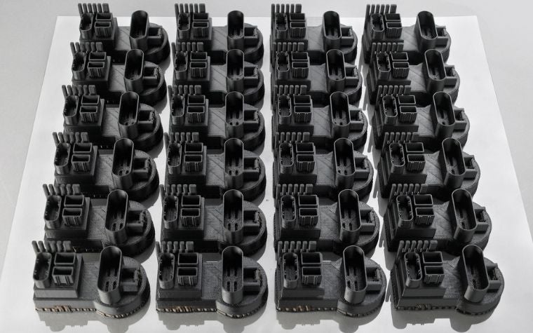 Eine Reihe identischer 3D-gedruckter Teile, die mit FDM hergestellt wurden, auf einem weißen Quadrat.