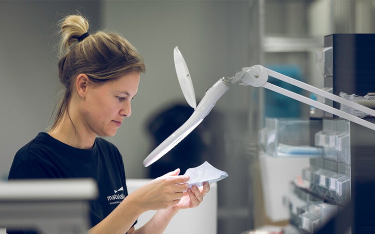 Mujer inspeccionando una pieza bajo una lupa en la zona de producción de Materialise.