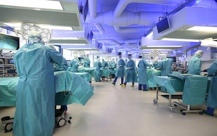 A large room in a hospital with various surgical table setups and surgeons in scrubs around each table