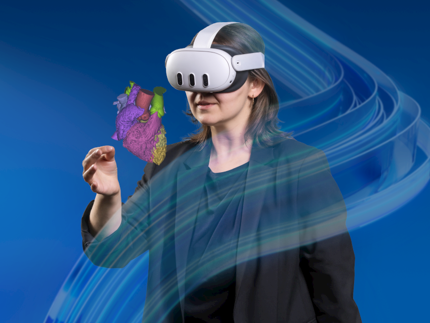 메타 퀘스트 3 XR 헤드셋을 착용한 여성이 분절된 심장 모형을 앞에 두고 있습니다. Mimics 브랜드 소용돌이가 전경에 흐릿하게 표시됩니다.