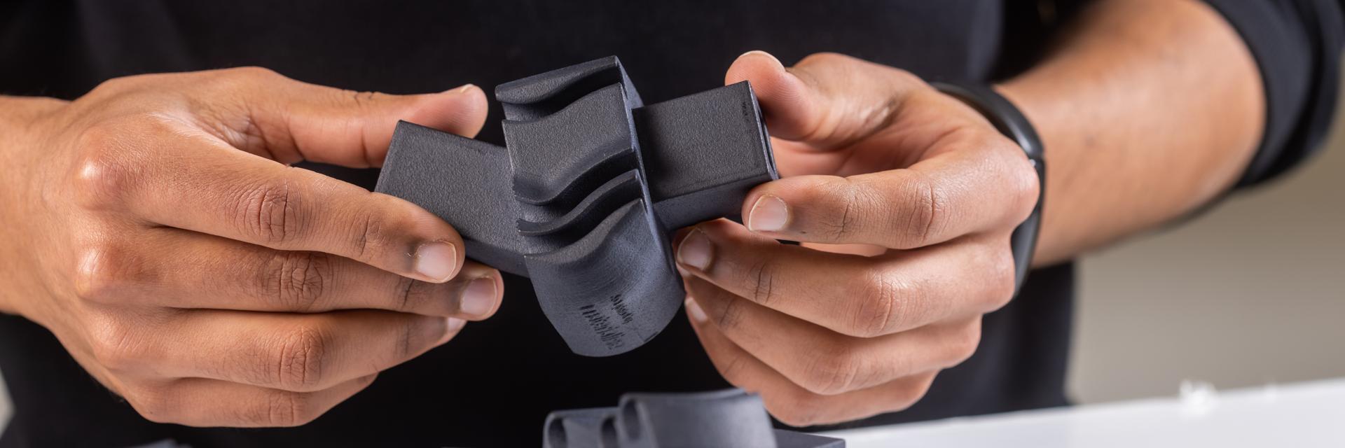 Les mains d'un homme tenant une pièce en plastique noir imprimée en 3D.