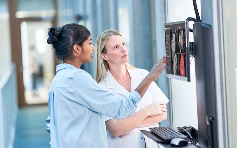 A medical technician and clinical engineer in a hospital hallway, looking at a monitor on the wall that displays Mimics