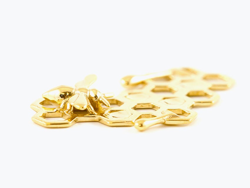 A gold charm in the shape of a honeybee and honeycomb made with lost-wax casting.