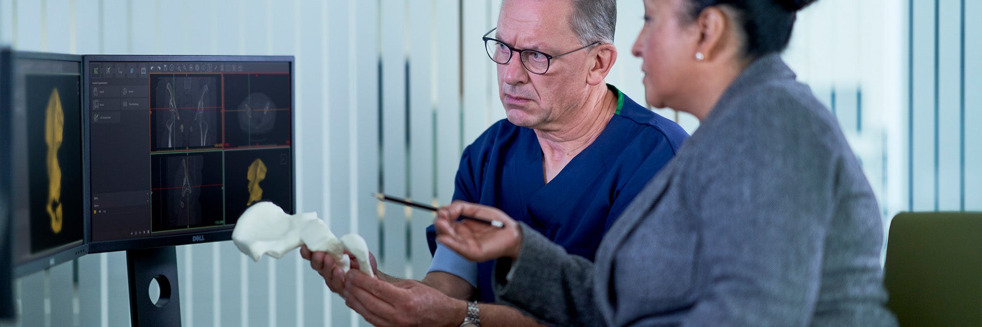 Two healthcare professionals looking at images of patient anatomy on computer screens while holding a 3D-printed anatomical model