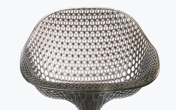 View of a geometrical, 3D-printed chair seat from a 3D-printed prototype of a customized, futuristic-looking wheelchair, using multiple 3D printing materials. The seat is lattice-structured and made of a translucent gray resin.