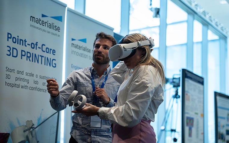 A man assisting a woman wearing a VR headset at a point-of-care 3D printing event
