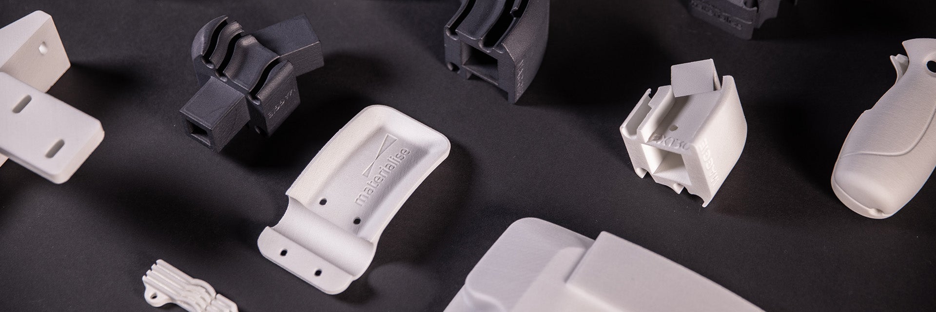 A selection of grey and white 3D-printed polyamide parts on a black felt background.