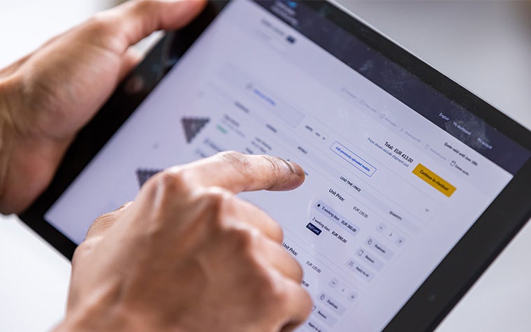 Hands holding a tablet, opened to the Materialise Manufacturing online ordering platform with the right index finger hovering over the screen