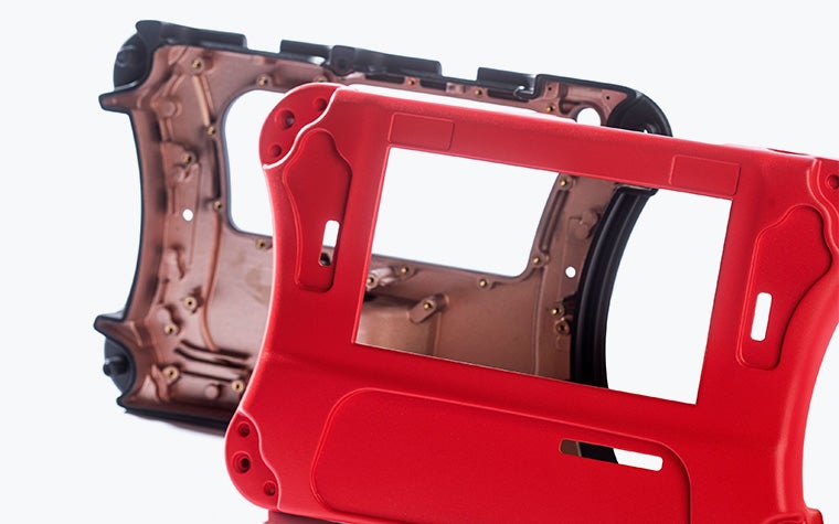 The front of a red vacuum-cast housing in front of the backside of the same part