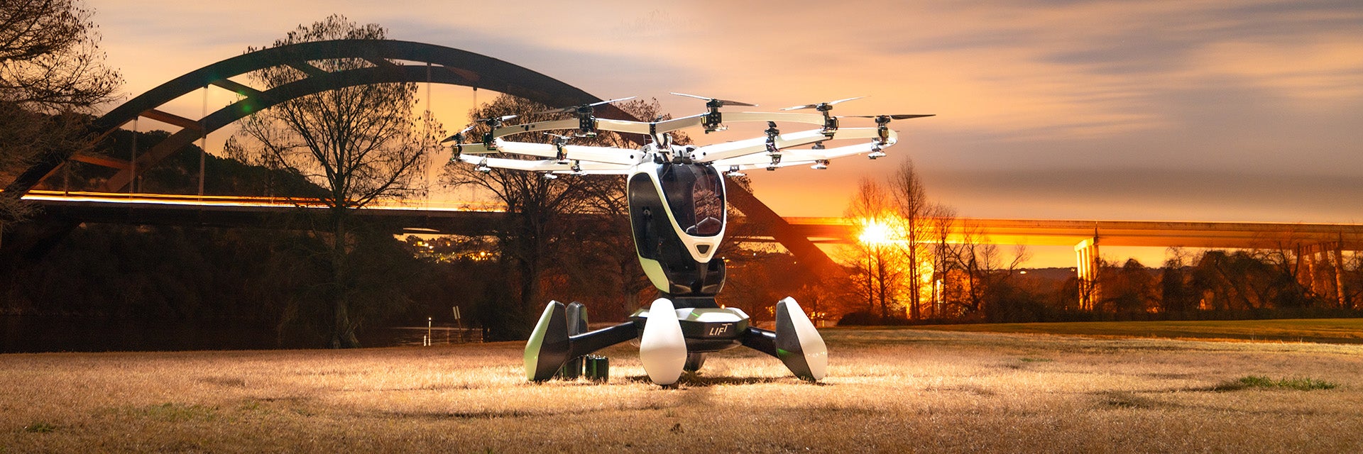 Das HEXA-Flugzeug von LIFT landet vor einer Brücke mit einem Sonnenuntergang im Hintergrund