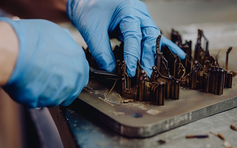 A production worker's gloved hands using a tool to remove support structures from metal 3D-printed parts