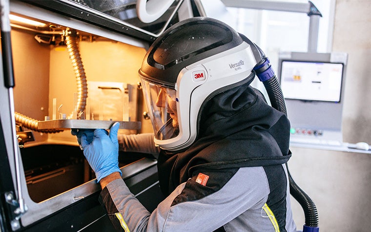 Man wearing safety gear and removing a build with metal 3D prints from a 3D printer