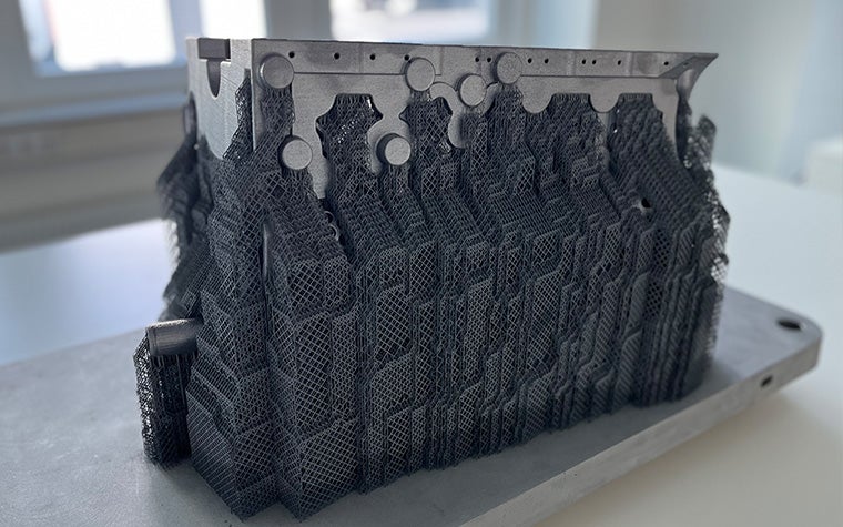 A metal 3D-printed crankcase produced by the BÖLLINGER GROUP sitting on a wooden table.