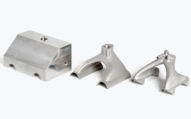 Three variations of the same metal gripper, one designed for conventional manufacturing, one sleeker one designed to be printed, and one even sleeker one with a design optimized for additive manufacturing