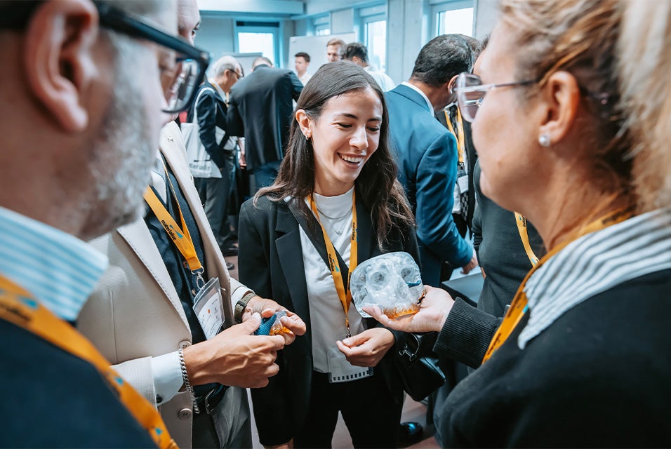 A woman at the Materialise CMF Innovation Summit in a room full of attendees, looking at a 3D-printed model of a skull