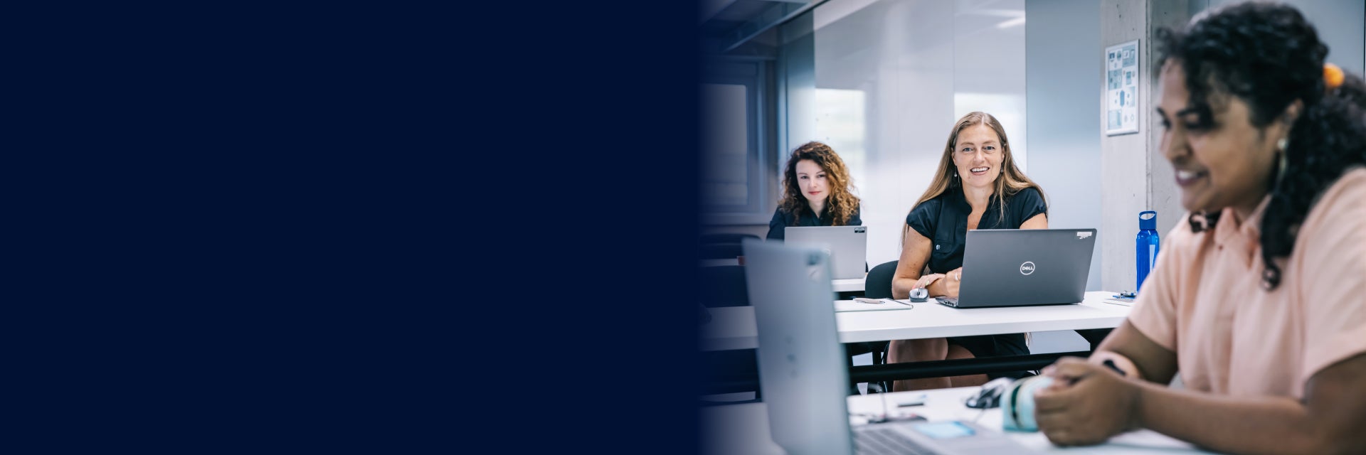 On the right is a woman sitting in a classroom looking at a laptop. Behind her are two women also looking at laptops and smiling. On the left is a bluish blur effect.