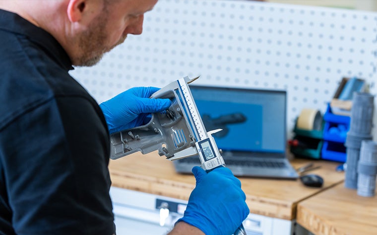 Un miembro del equipo de calidad de Materialise sostiene un calibre para medir una pieza impresa en 3D.