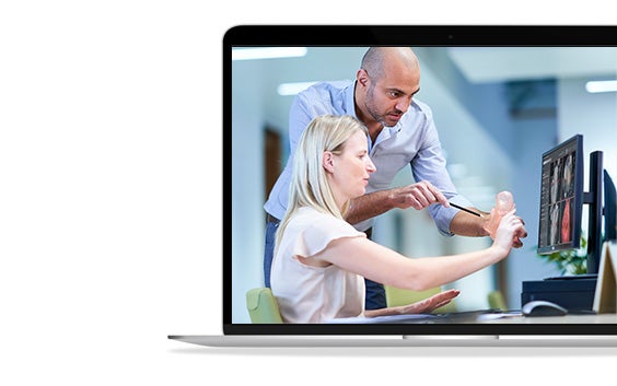 Pantalla de ordenador portátil que muestra a una mujer sentada y a un hombre de pie, ambos mirando un modelo anatómico delante de una pantalla de ordenador.